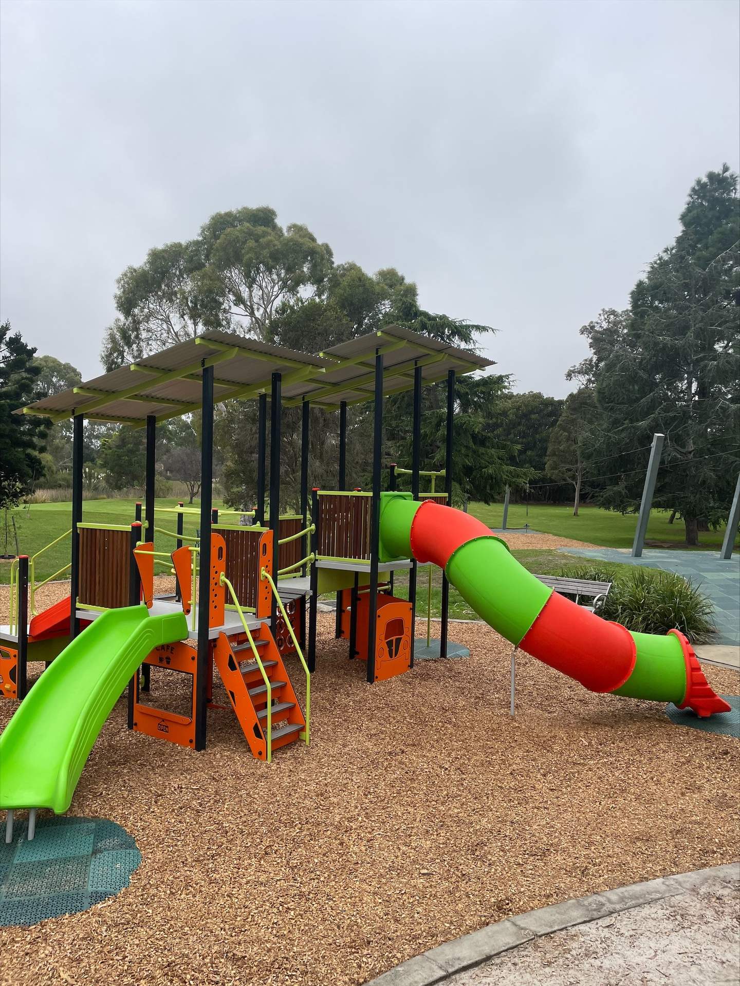 Colourful slides and multiplay station in playground with trees grass and tan bark