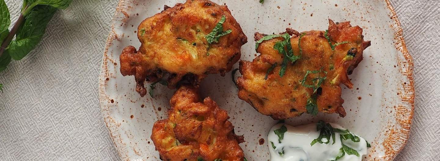 Vegetable fritters on a plate with with a side of creamy sauce and some garnish 