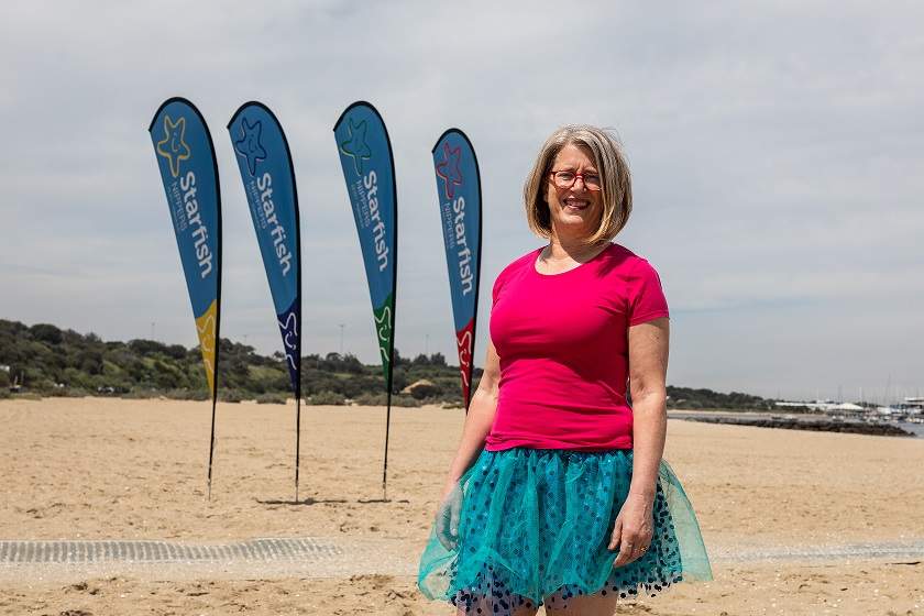 Kerrie wears a pink top and blue tutu standing in front of Starfish banners