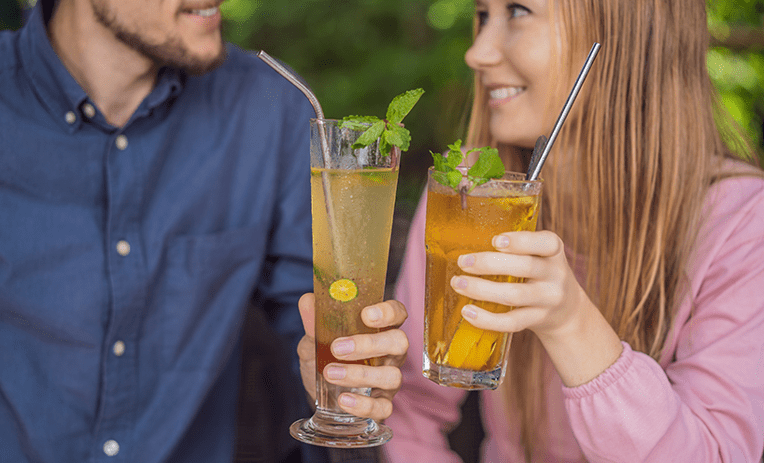 Two people smiling at each other while holding two cocktails with reusable straws in them