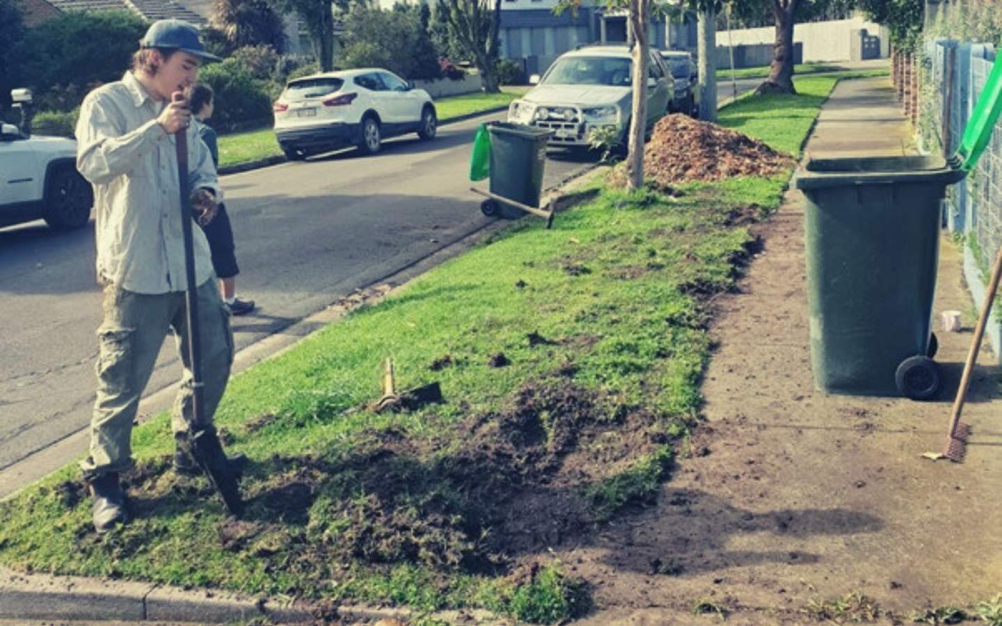 Teenager digging up nature strip reading for planting