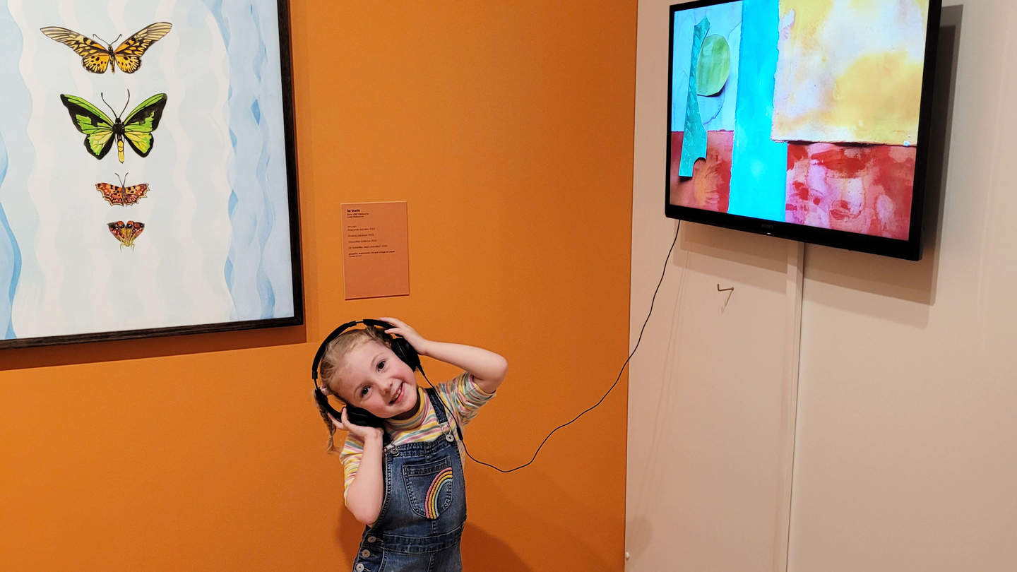 Little girl wearing headphones and watching an animation at Bayside Gallery.