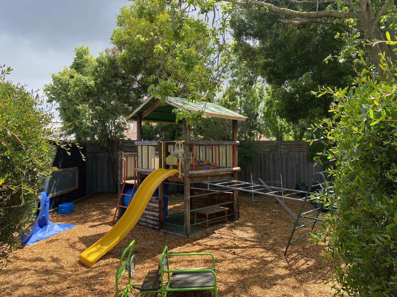 Playground with slide amongst tanbark and green garden at Hampton Community Kindergarten