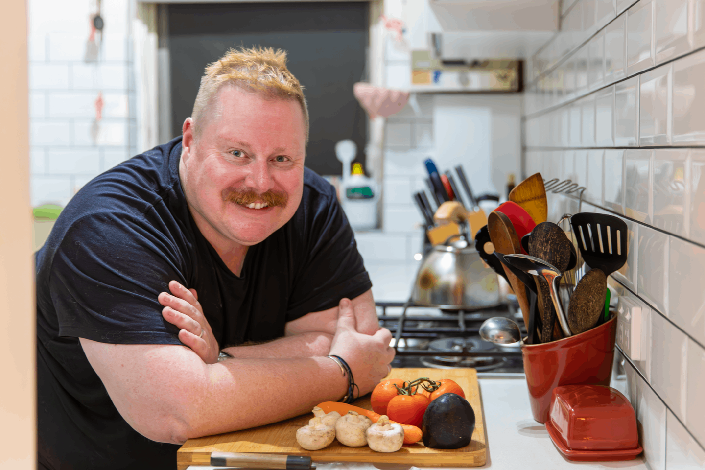 Man smiling with elbows on bench in front of food and cooking utensils