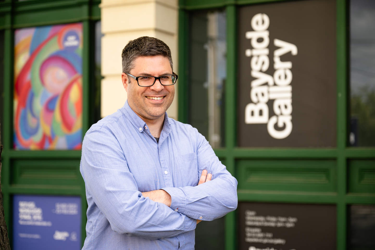 Brown haired man with glasses smiling with folded arms in front of Bayside Gallery sign