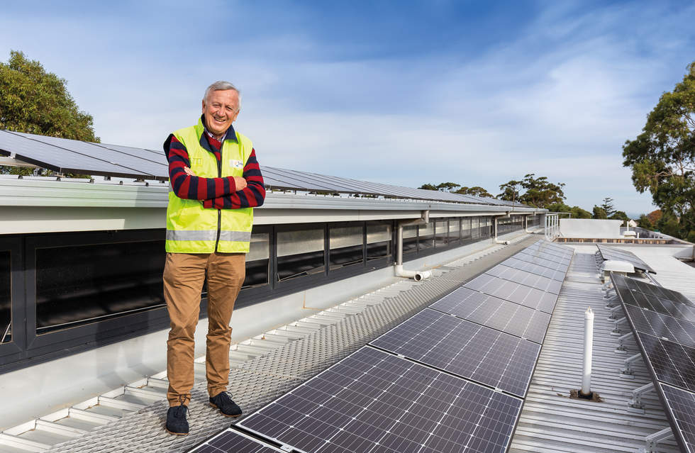 Bayside Mayor Laurie Evans in a high vis yellow vest standing on the roof of Bayside City Council corporate centre next to rows of Solar panels on the roof. 