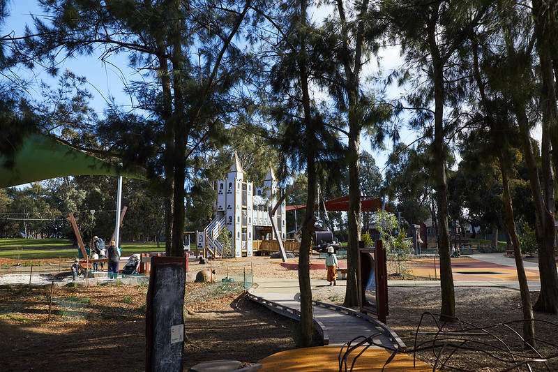 A view through the trees into Thomas Street all-inclusive playground where children are playing