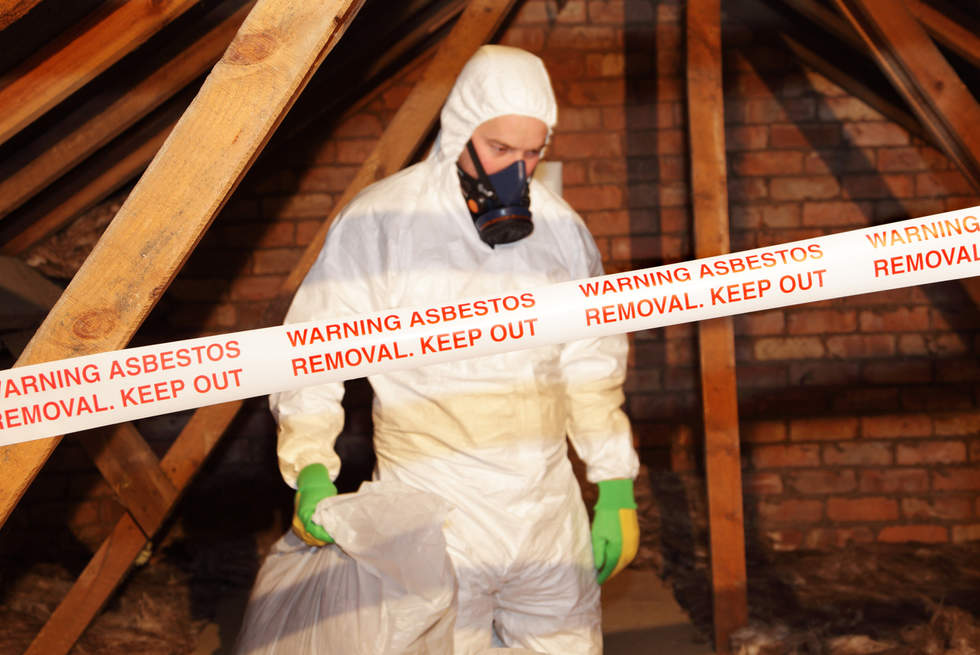 Masked and suited asbestos removal expert in an attic