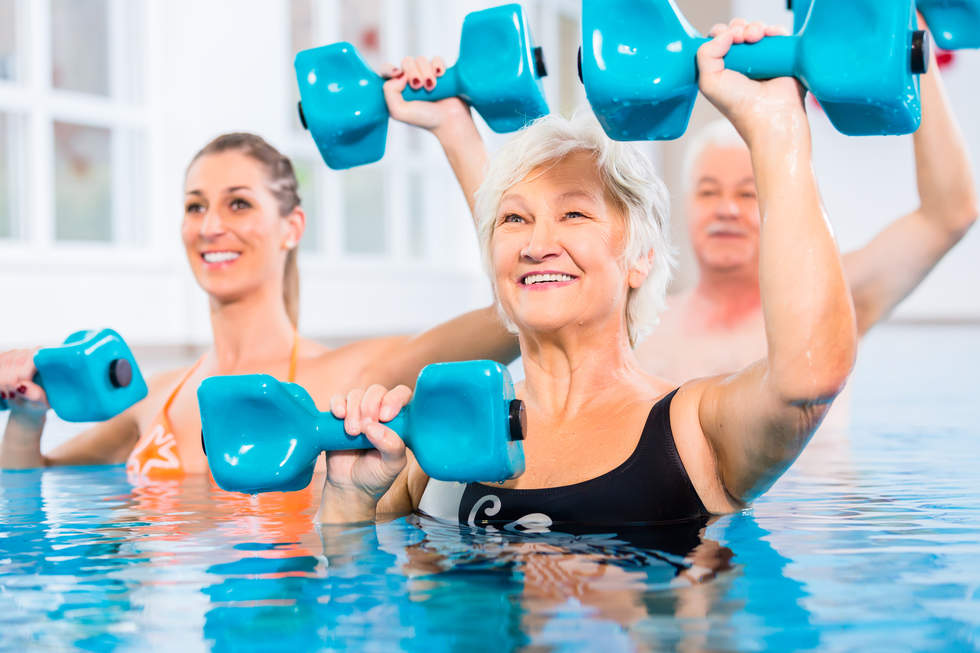 Three adults exercising with blue weights in a warm water pool