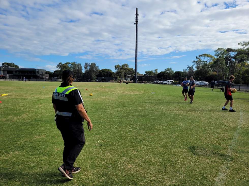 A uniformed Local Laws officer watches a ball game at a sports ground