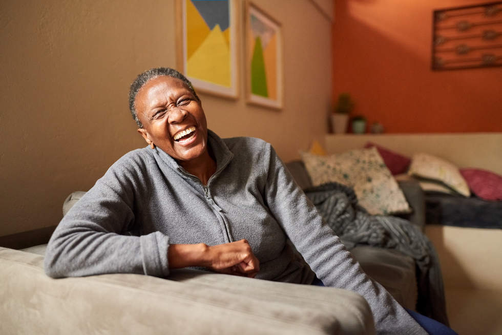 Portrait of a cheerful senior woman sitting on sofa in the living room and laughing
