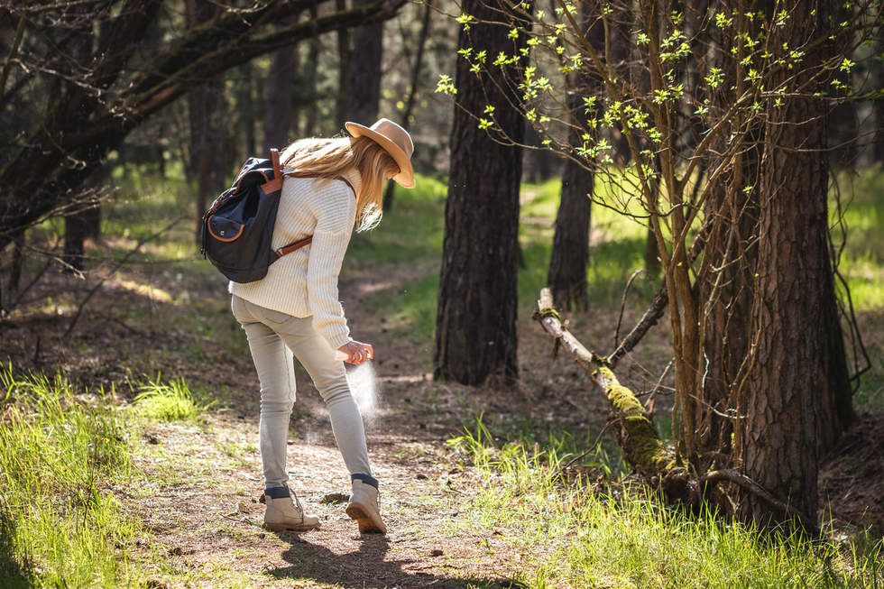 Woman in walking gear in a forest spraying her legs