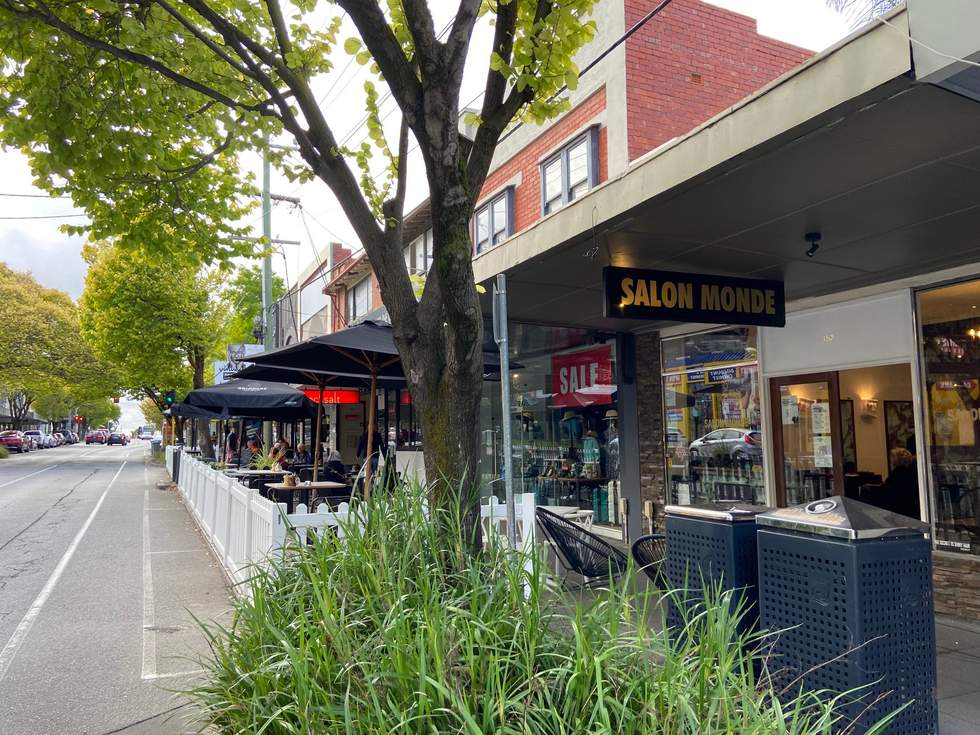 Parklet with picket fence, trees footpath, road, shops, tables, chairs
