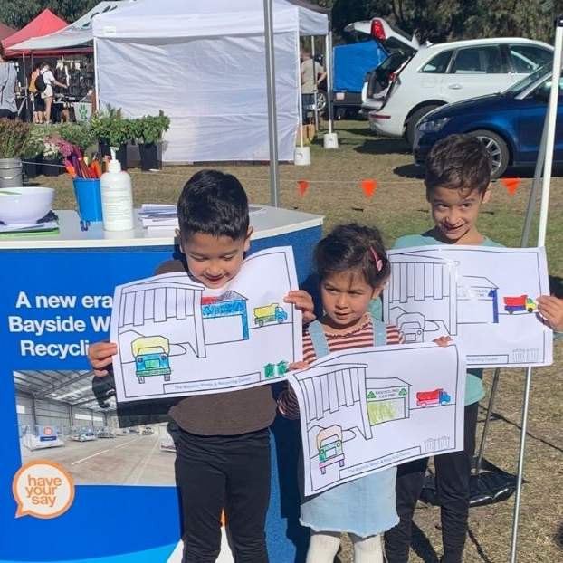 Three cute children with colouring in pages outside Have Your Say tent