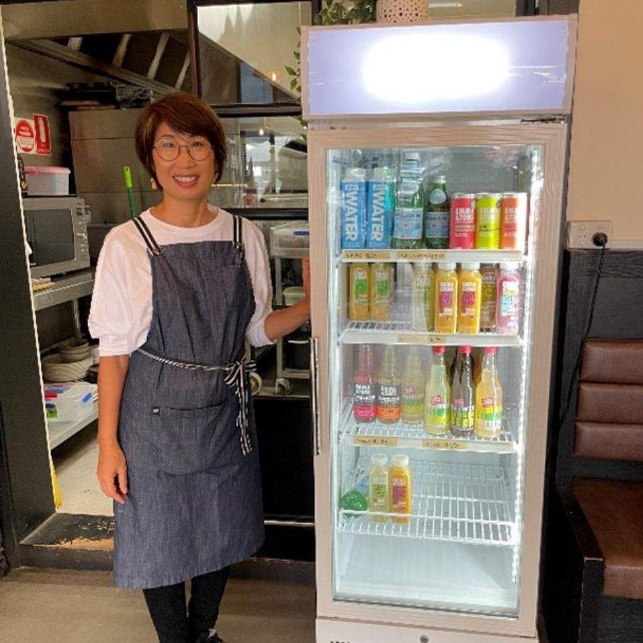 Woman in apron standing next to new fridge in cafe