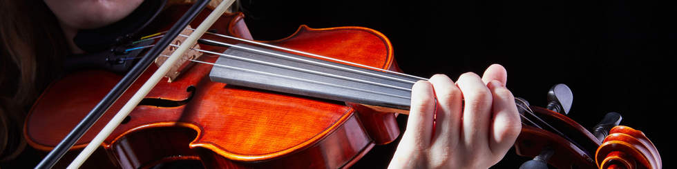 Close up view of someone playing the violin. The colour of the violin is vibrant against a black background.