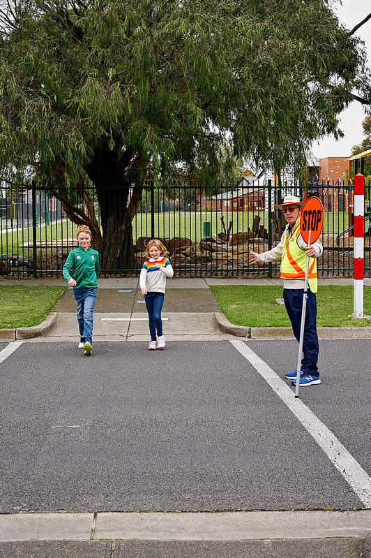 Two children cross the road under the supervision of a friendly school crossing supervisor wearing high vis