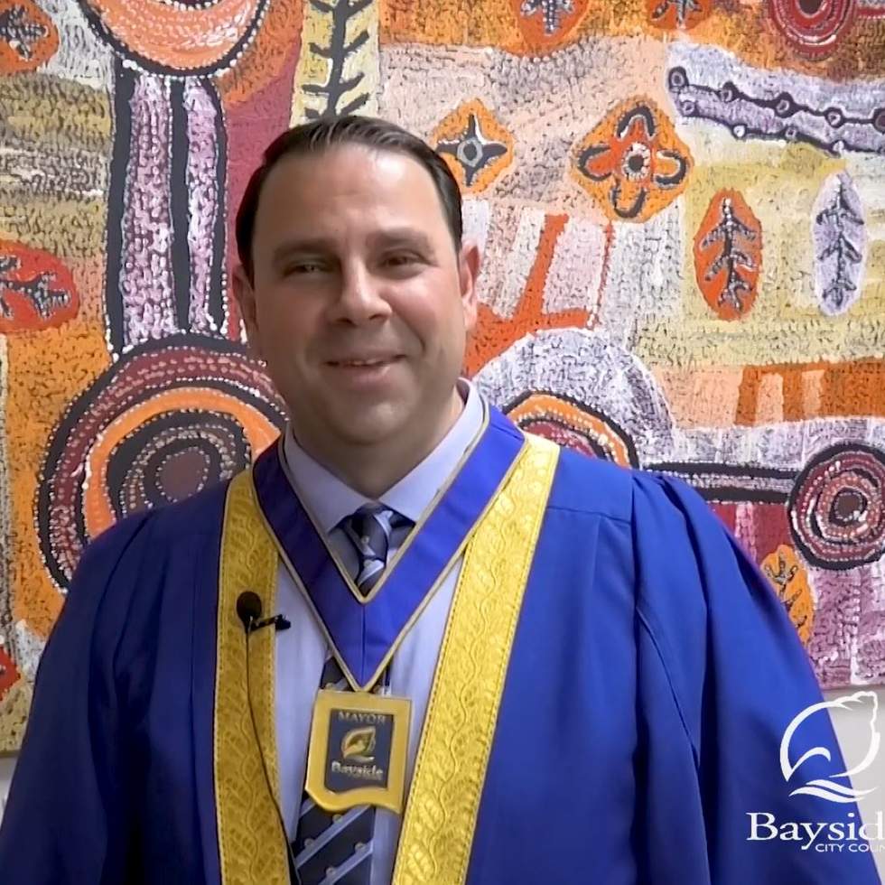 Cr Hanna El Mouallem, wearing Mayoral robe, in front of an aboriginal painting