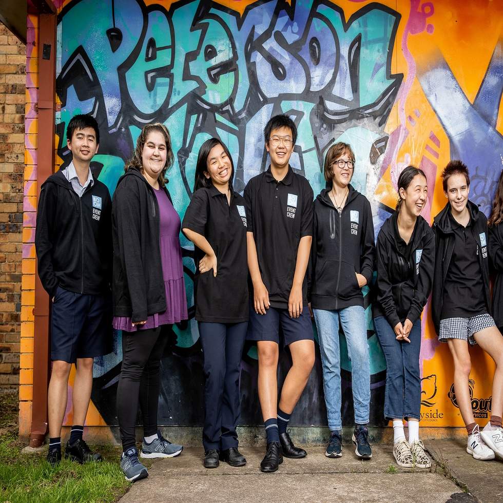 8 member of Bayside's Youth Advisory Committe smiling in front of graffiti that reads 'Peterson Youth Centre'