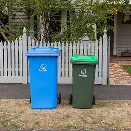 Light blue recycling bin on curb next to dark green, light green food and green waste bin