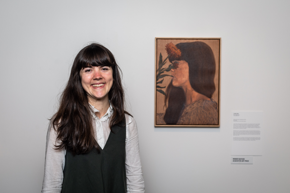 Woman with brown hair smiling in front of self portrait painting