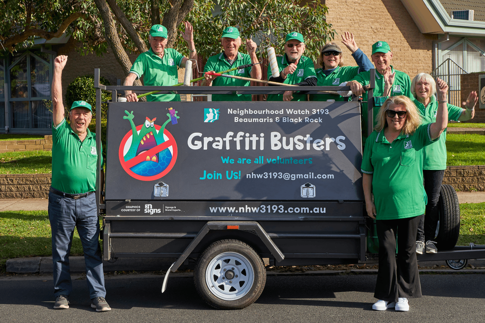 Graffiti Busters volunteers wearing green cheering in front of graffiti removal trailer
