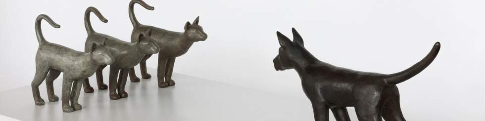 Bronze art sculpture of three cats standing opposite a big dog with tails up in the air