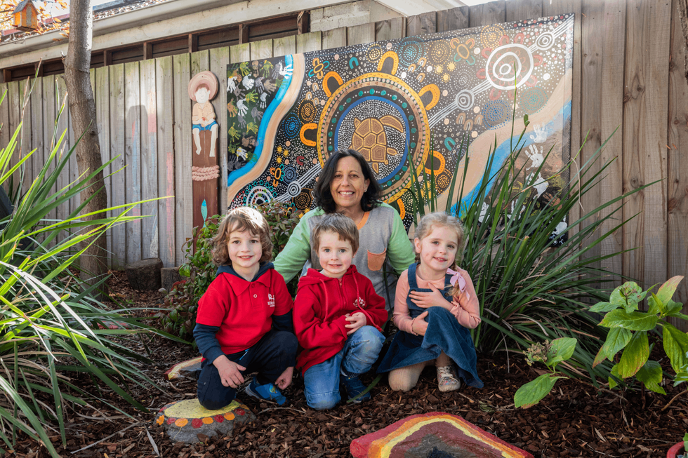 Three children and woman stand in front of Aboriginal artwork