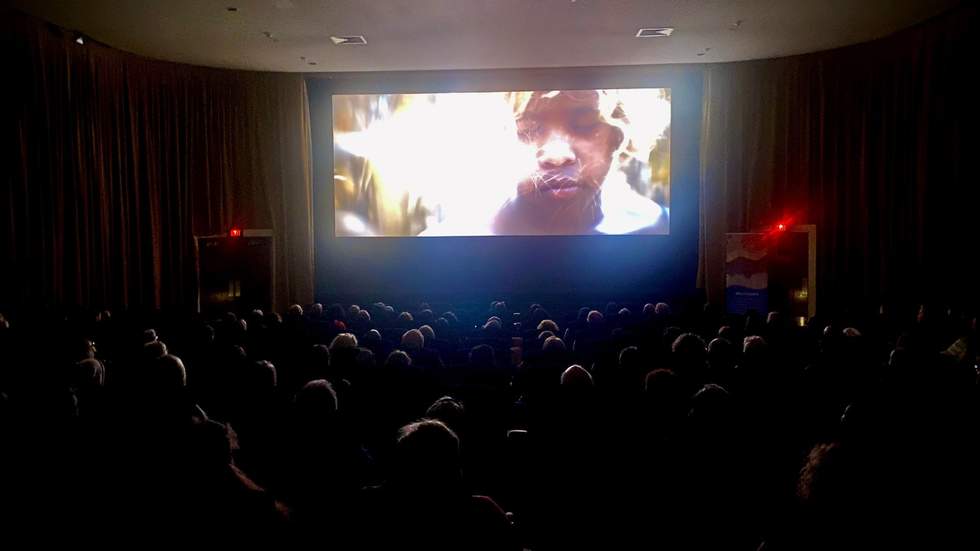 Crowd in a cinema. Movie screen has a boy's face and fireworks.