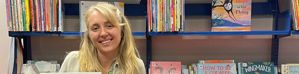 Young librarian smiling to camera in front of shelves of books