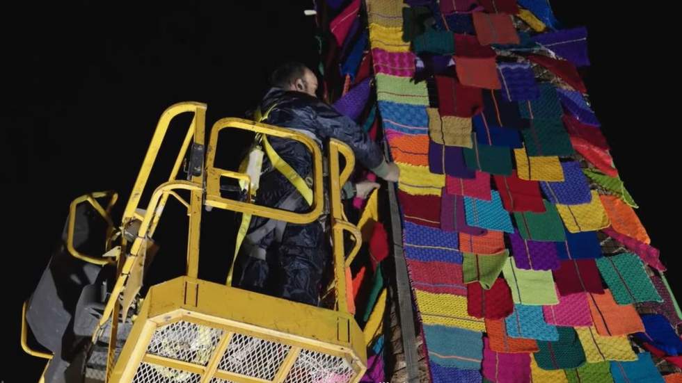 Close up of man on cheery picker installing small knitted squares on the Black Rock Clock Tower at night.
