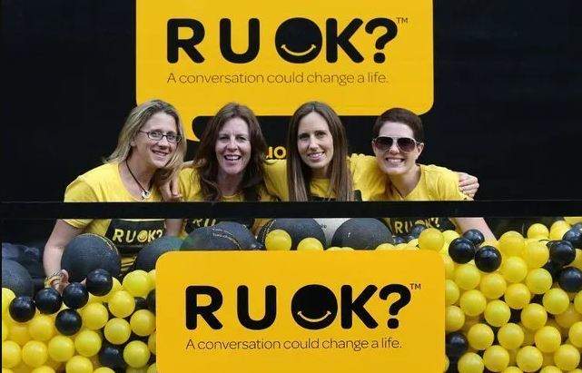 Four women in yellow t-shirts beside R U OK? Day posters.