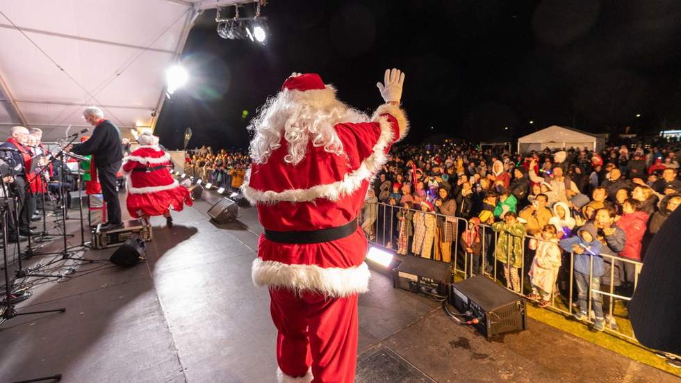 Santa on stage at carols waving at crowd.