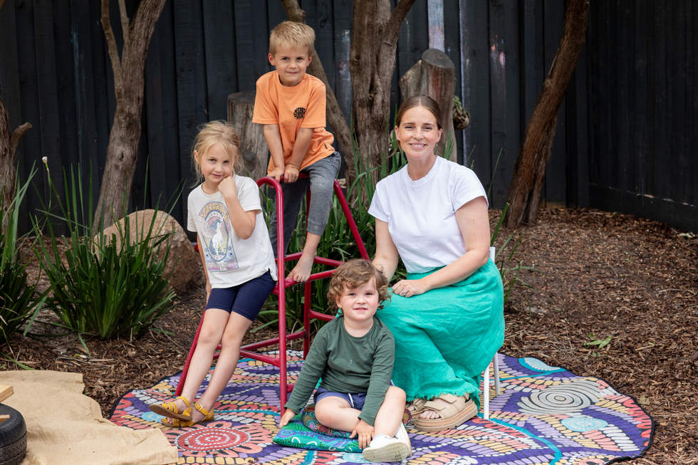 Ellie and children from Bayside Playhouse sitting in garden with tambark and trees in the background