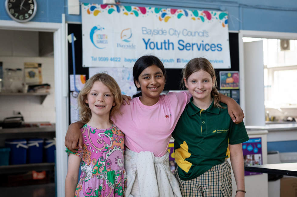Three girls smiling in front of Bayside City Council Youth Services sign