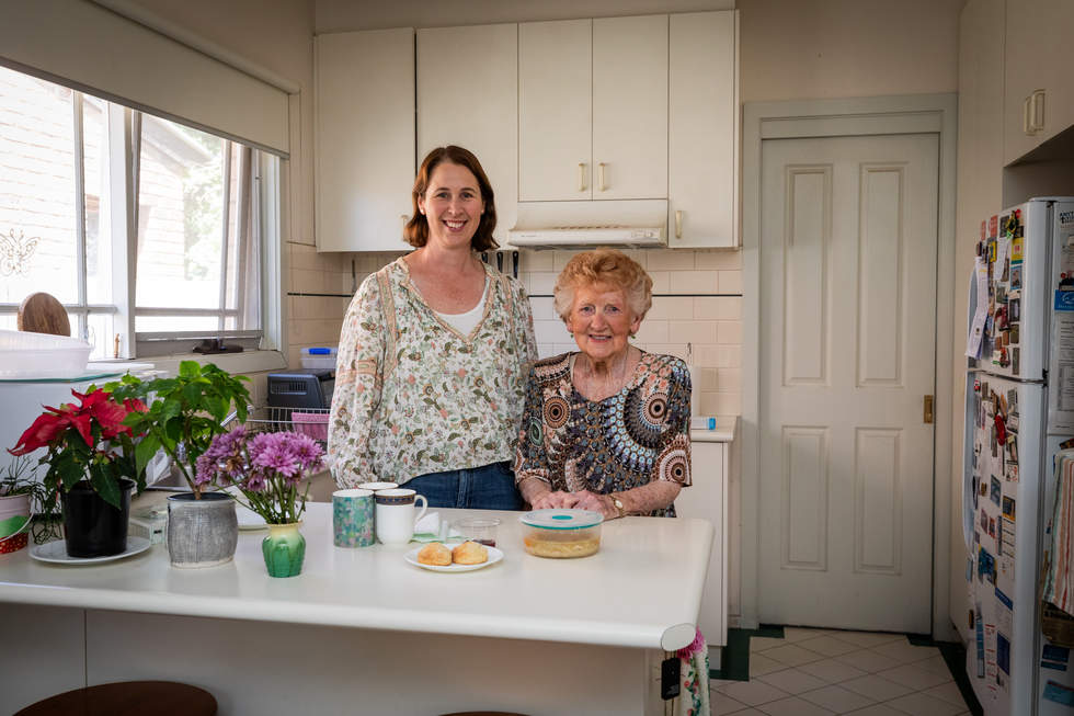 Two women smiling in front of a kitchen bench